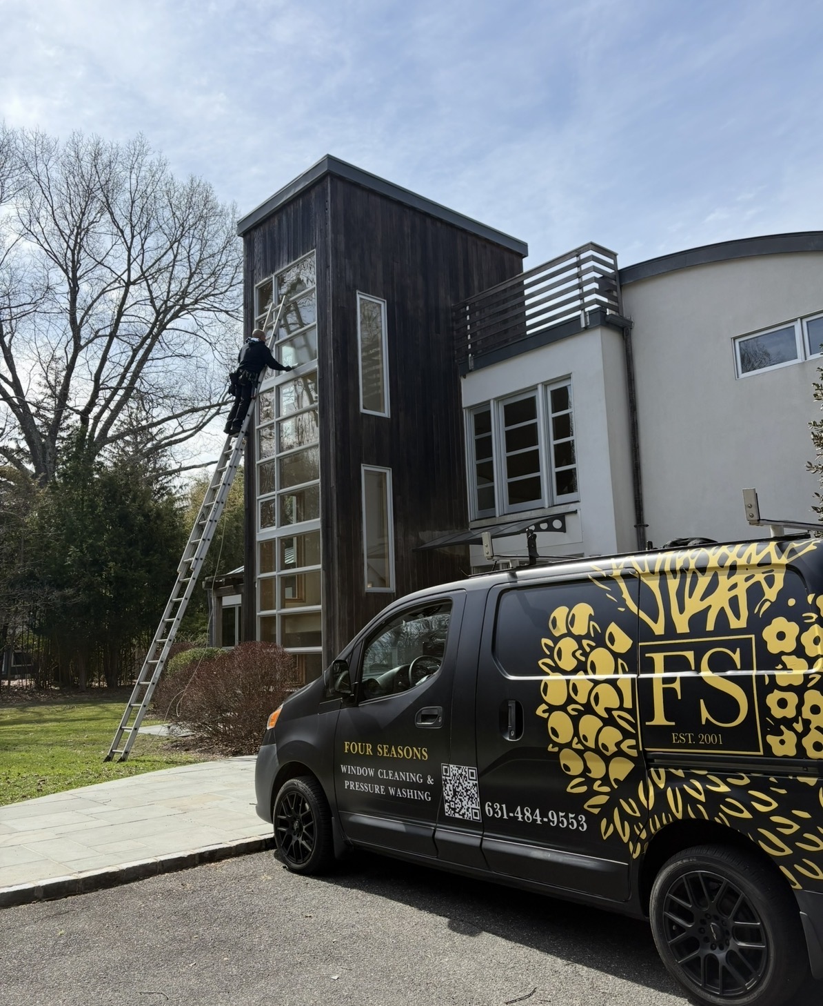 Four Seasons cleaning tall windows with the black-and-gold company van in front of the home